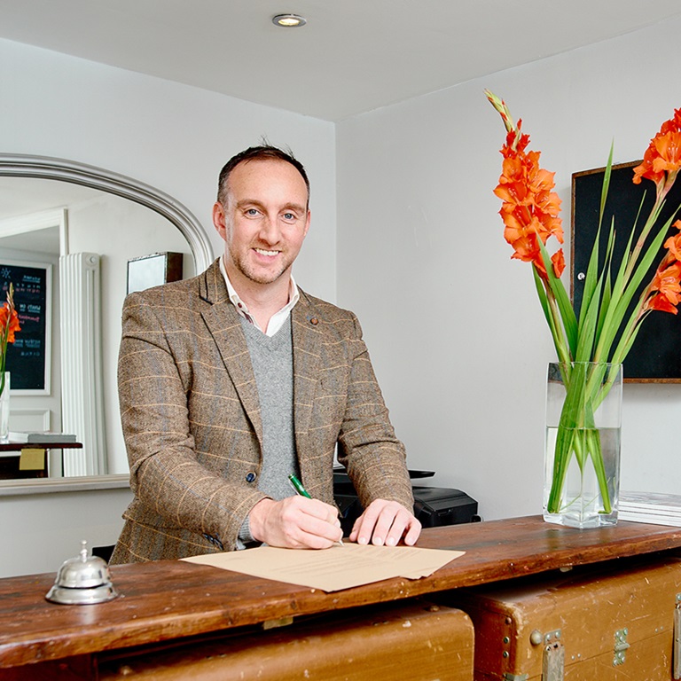 Lawrence Hotel front desk made of old luggage, man in tweed jacket smiling and signing papers