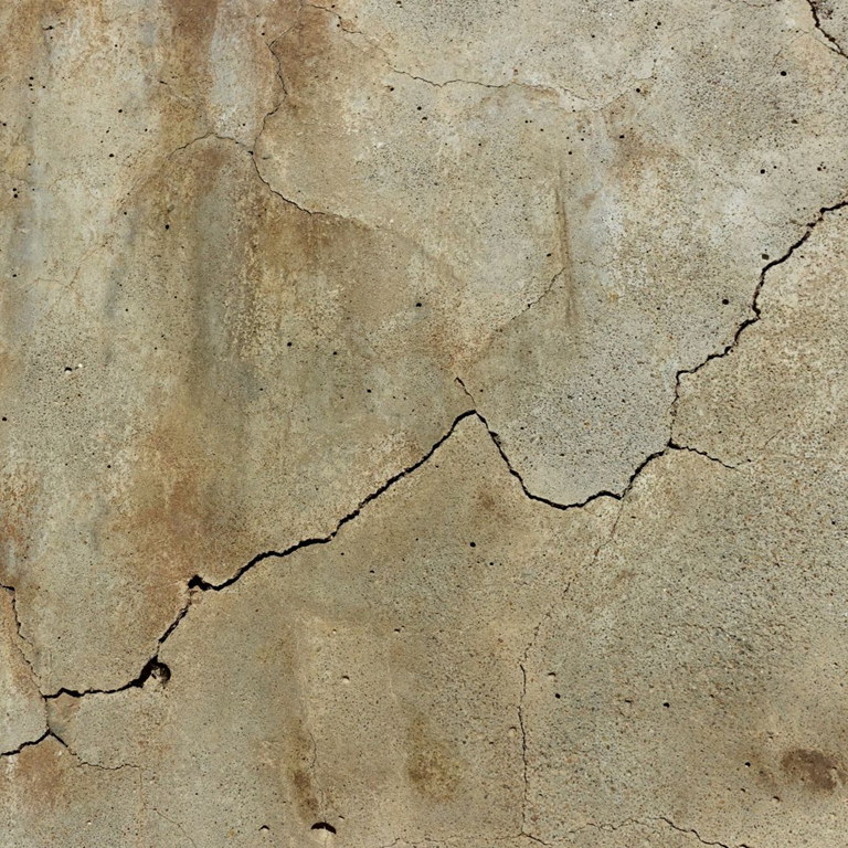Close-up image of a cracked and damaged concrete wall showing multiple fractures and surface deterioration.