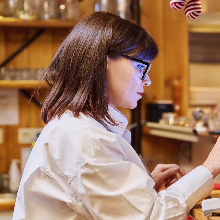 Woman wearing glasses uses a digital screen at a restaurant counter, illustrating cyber for hospitality.