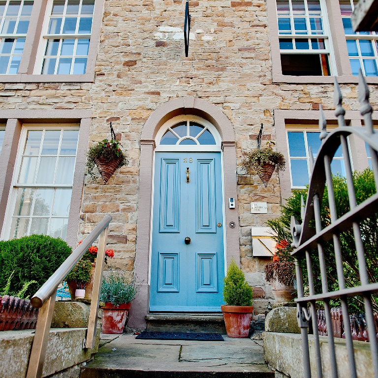 Hotel safety view of a stone building entrance with a blue front door, steps, railings, and potted plants.