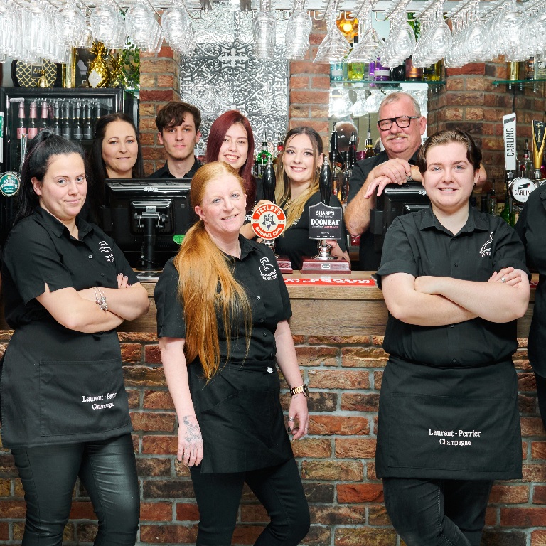 Pub staff standing behind a bar in a licensed venue, illustrating Tenant vs Freeholder Pub Insurance Responsibilities