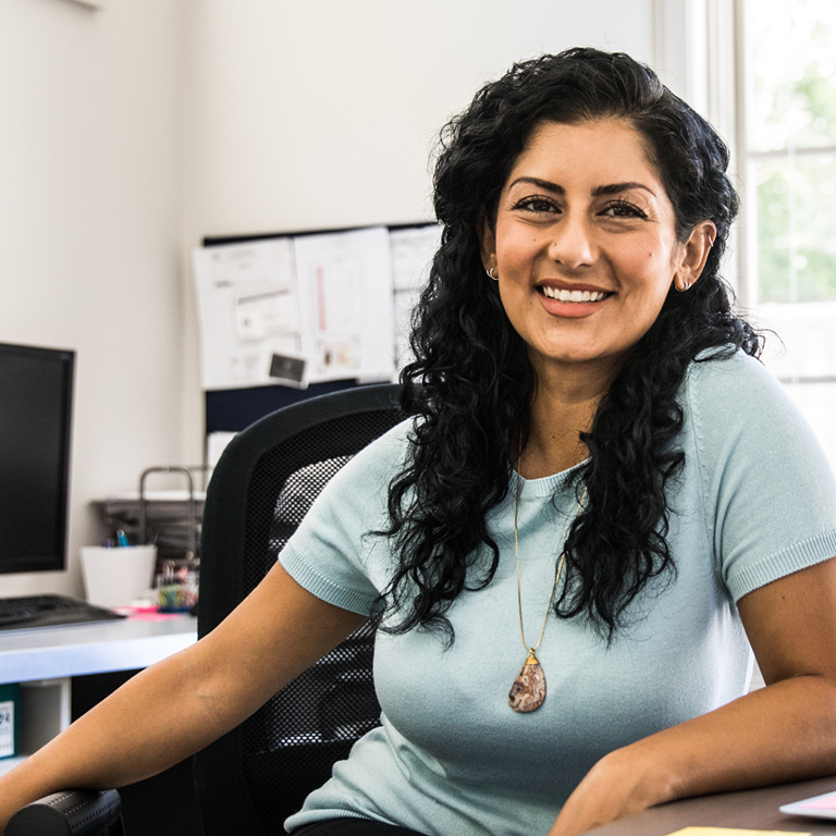 A lady smiling at her office desk in a small team office.