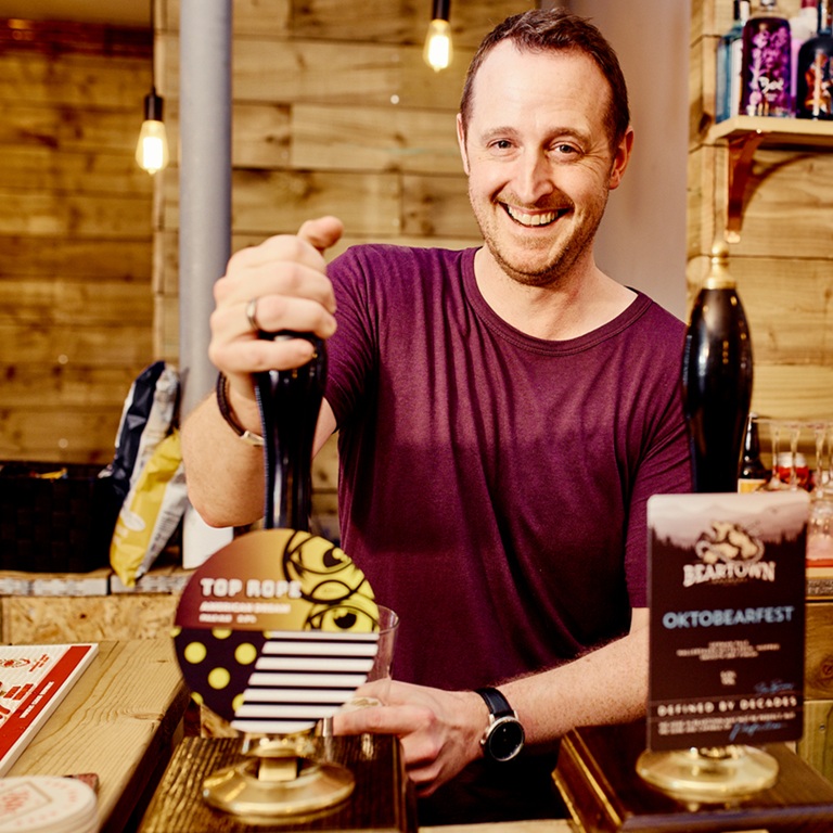 Freehold Pub Insurance Guide showing a smiling pub owner behind the bar with beer taps and a pub interior in the background.