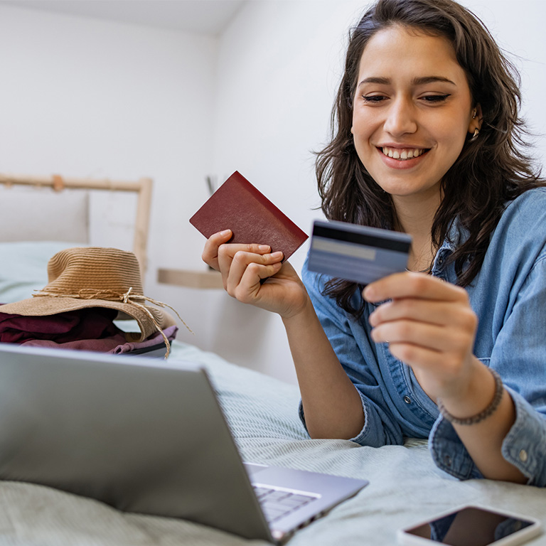 Woman using a laptop and holding credit cards in a guesthouse setting, highlighting guesthouse cyber risk for bookings, payments, and data.