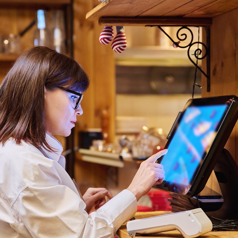 A woman using a point-of-sale system in a restaurant, showing restaurant cyber insurance for POS and delivery platforms.