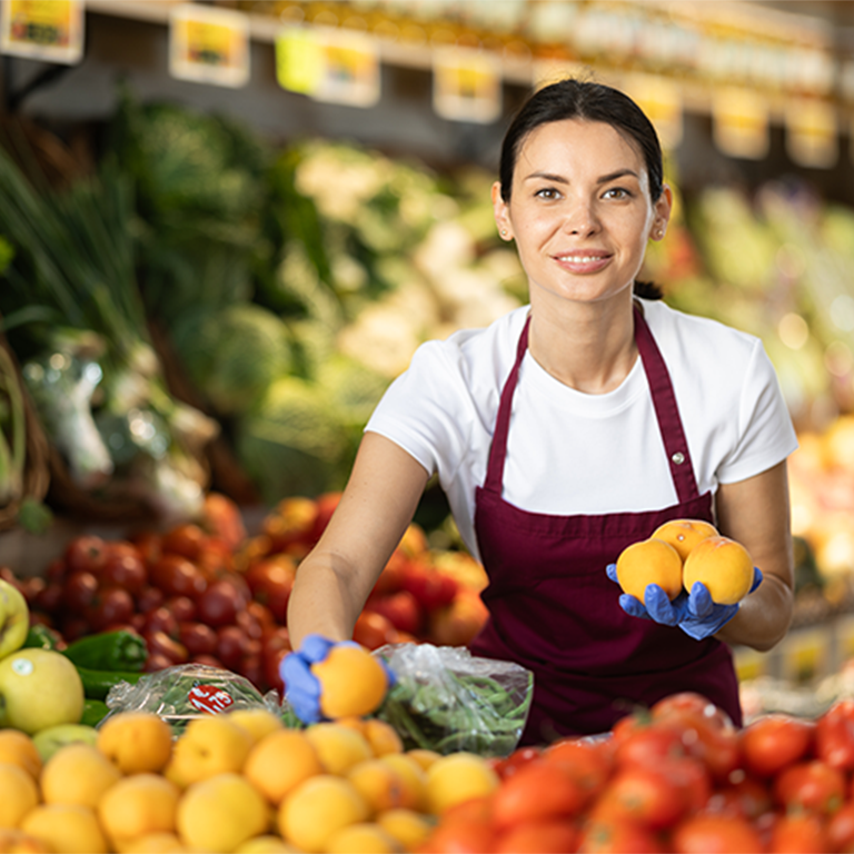 A woman holding oranges at a fresh produce market, illustrating seasonal trading for restaurant insurance and outdoor dining.