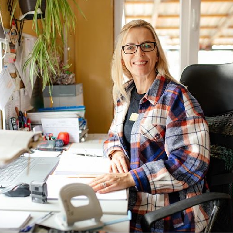 A person sitting at a desk with a laptop, paperwork, and office supplies in a bright home office, representing self employed finance and work management
